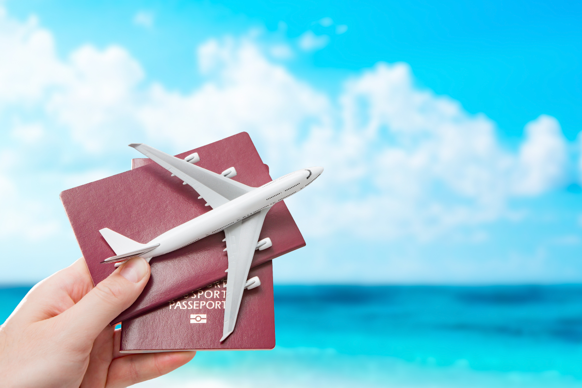 une main montre deux passeports rouges avec un avion miniature sur fond bleu
